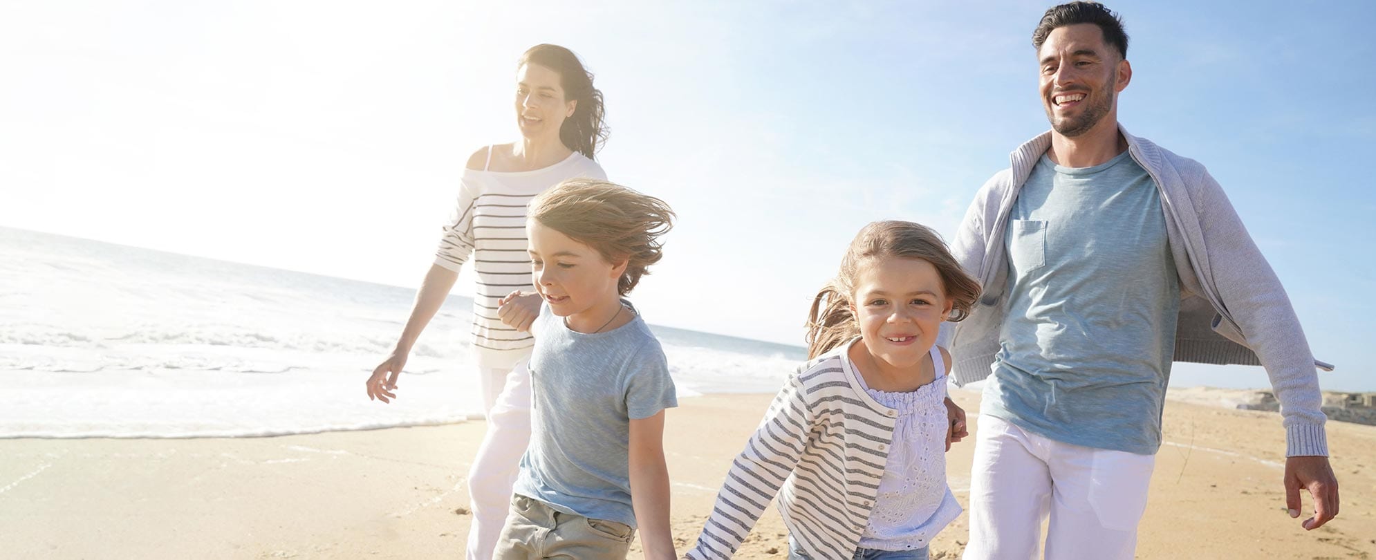 Happy family of four all holding hands while running on a beach shoreline 
